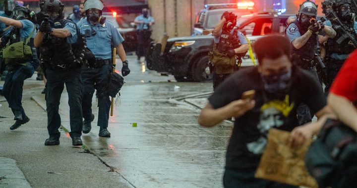 Protestors in the foreground run away from police officers in the background