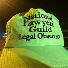 A green National Lawyers Guild Legal Observer hat is shown at night