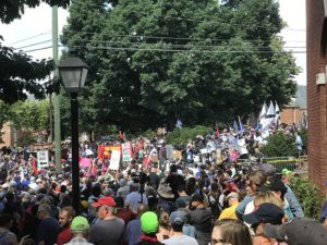 A large crowd of anti-racist protestors face off against white supremacists on a tree-lined street. Only the tops of most people's heads are visible. there are two neon hats in the crowd. They are National Lawyers Guild legal observers.